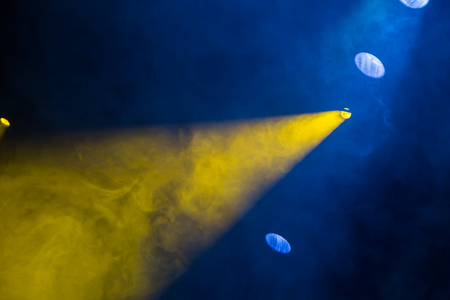 Yellow and blue light rays from the spotlight through theatrical smoke. Lighting equipment on the stage.の写真素材