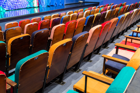 The auditorium in the theater. Blue-green curtain on the stage. Multicolored spectator chairs. Lighting equipment.の写真素材