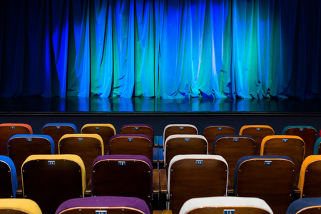 The auditorium in the theater. Blue-green curtain on the stage. Multicolored spectator chairs. Lighting equipment.の写真素材