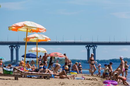 Saratov / Russia - July 6, 2018: People sunbathe and swim in the sandy beach. On a sunny summer day. Road bridge on the horizon.のeditorial素材