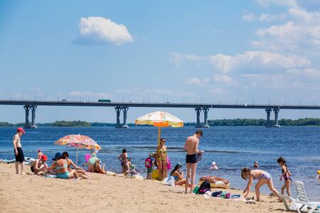 Saratov / Russia - July 5, 2018: People sunbathe and swim in the sandy beach. On a sunny summer day. Road bridge on the horizon.のeditorial素材