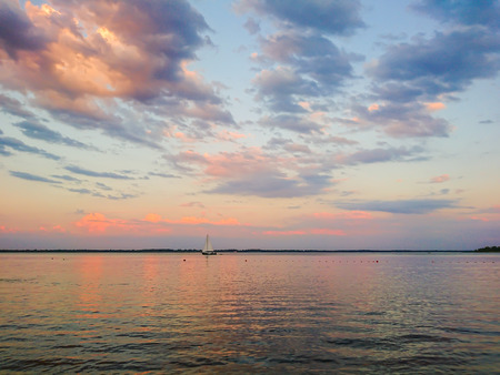 Picturesque river landscape. Sunny sunset. Pink clouds on the blue sky. Sailboat on the horizon.の写真素材