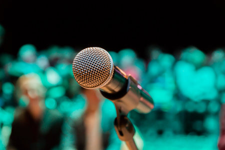 Wireless microphone on the stand. Blurred background. People in the audience. Show on stage in the theater or concert hall.の写真素材