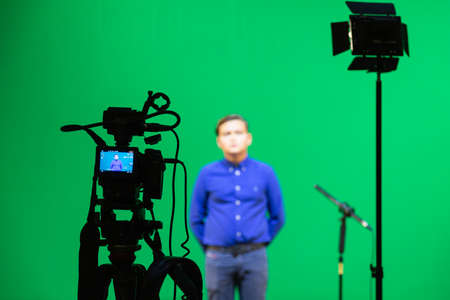 Videography of a boy in a blue shirt in the studio on a green background. Chromakey technology. A microphone on a stand, a video camera on a tripod and lighting equipmentの写真素材