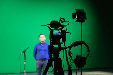 Videography of a boy in a blue shirt in the studio on a green background. Chromakey technology. A microphone on a stand, a video camera on a tripod and lighting equipment.の写真素材