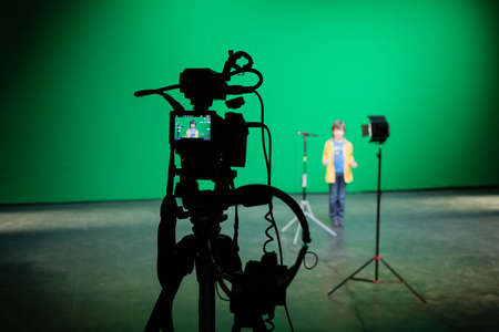 A boy on stage. Video shooting in the pavilion on a green background. Filming equipment: camera, microphone, tripod, spotlight, headphones, chromakey.の写真素材