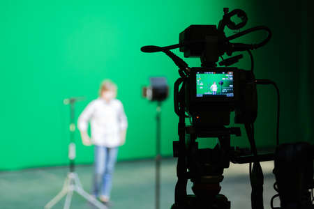 A boy on stage. Video shooting in the pavilion on a green background. Filming equipment: camera, microphone, tripod, spotlight, headphones, chromakey.の写真素材