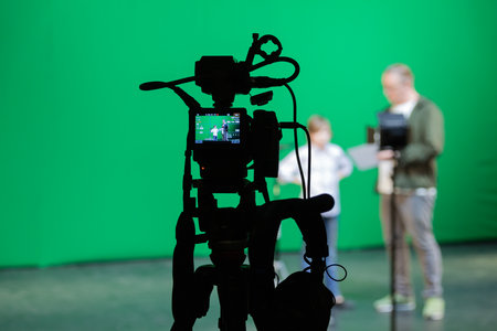 A boy and a director on stage. Filming on a green background for special effects. Shooting equipment: camera, tripod, chromakey, microphone, spotlight, headphonesの写真素材