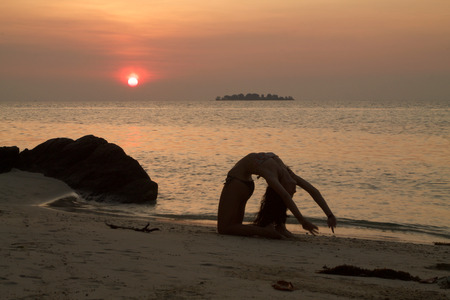beautiful young woman makes gymnastic exercises on the beach on sunsetの写真素材