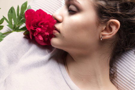 close portrait of beautiful girl lying with red flower near the faceの写真素材