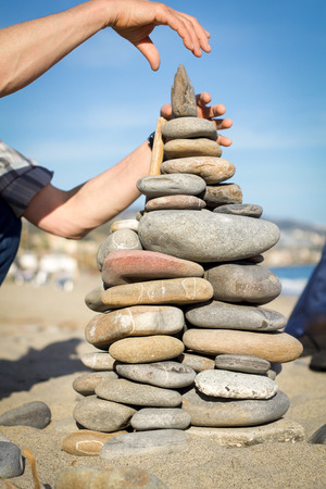 man's hands makes pyramid of stones on the sandの写真素材