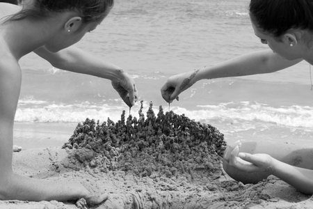 two young woman playing with sand on the beachの写真素材