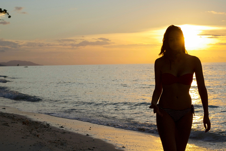 silhouette of young woman walking by the sea at sunset with a beautiful yellow shadesの写真素材