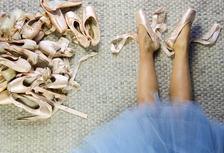 legs of female dancer lying with pointe shoes loose, near a group of used pointe shoesの写真素材