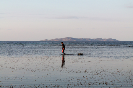 young man walking and fishing on the low tide in Kanawa island, indonesiaの写真素材