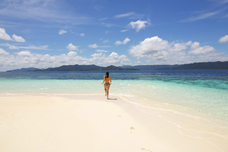 young woman running on a wild atoll towards the sea, raja ampat west papuaの写真素材