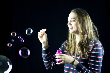 blond teenager doing soap bubbles smiling, black, backgroundの写真素材
