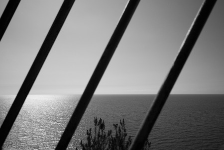 seascape with sun reflections in the sea  through iron bars, black and whiteの写真素材