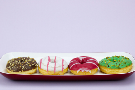 four  fresh colored donuts in a tray isolated on lilac backgroundの写真素材