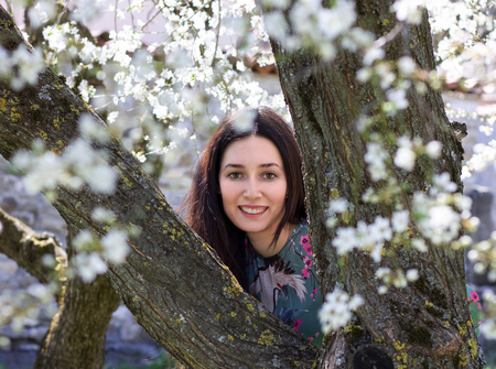beautiful young woman portrait smiling happy between branches of tree in bloom, concept of purity