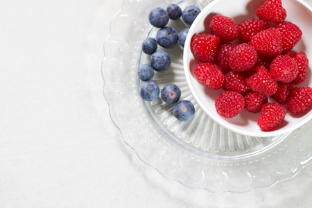 fresh raspberries in a white cup on a glass plate isolated, copy space