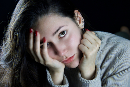 portrait of a sad girl lying down holding her head in her handsの写真素材