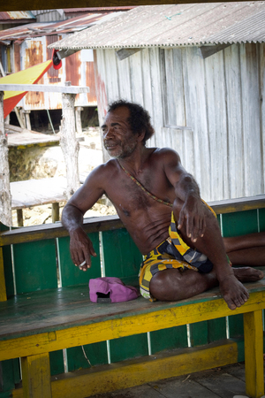 WEST PAPUA, RAJA AMPAT - August 28, 2017:portrait of unidentified  man that leave in a village of  Fam islands sitting ona wooden pier, smoking,  Raja Ampat archipelagoのeditorial素材