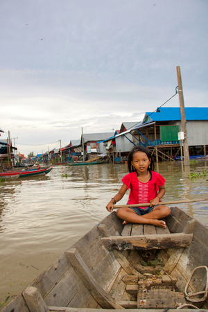 SIEM REAP Kampong Plug - September 7, 2018: unknown young cambodian girl sitting on a wooden boat accompanies tourists to visit the mangrove forest, floating village on the backgroundのeditorial素材