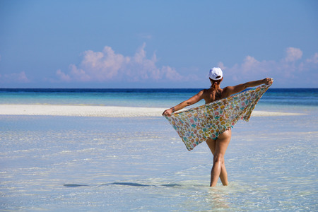 woman walking in a tropical sea playing with a colored pareo, exotic travel conceptの写真素材