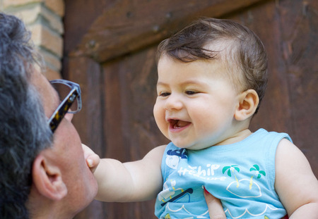 close portrait of beautiful smiling baby boy playing with his grandfatherの写真素材