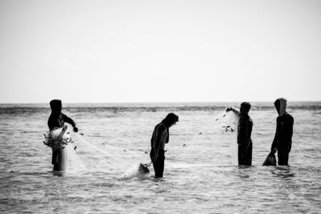 Maratua island, Borneo - August 29, 2018: silhouettes of  four asian boys move fishing nets standing...