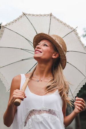 young woman with white lace umbrella, white dress and country straw hat smiling in the natureの写真素材