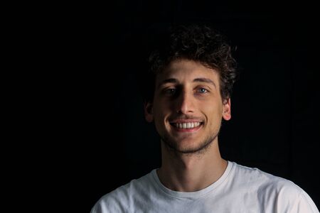 portrait of smiling guy in white shirt on black backgroundの写真素材