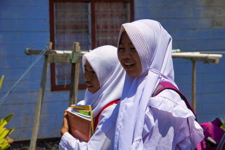 Borneo, Kalimantan -September 4, 2018: two young girls in school uniform with books and backpack leave school and walk homeのeditorial素材