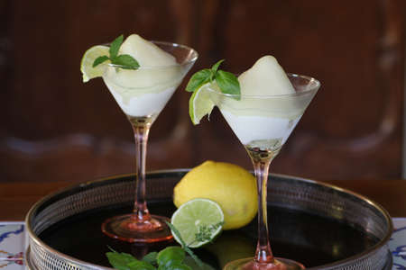 two cocktail glasses of lemon sorbet flavored with basil and lime on black trayの写真素材