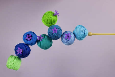 balls group of cotton yarn in the shades of blue and green and small purple flowers near a knitting...