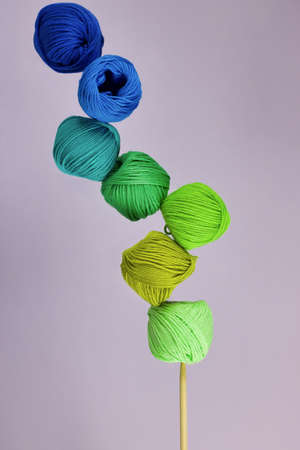 group of cotton balls yarn in the shades of green and blue in balance on wooden knitting needle,...