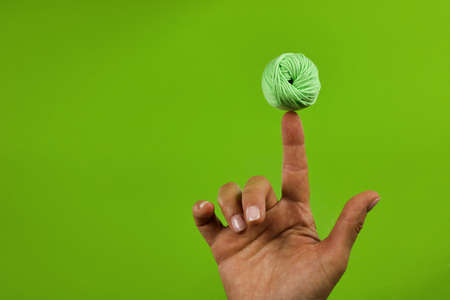 green cotton ball in balance on female finger, concept of leisure of knitting, green backgroundの写真素材