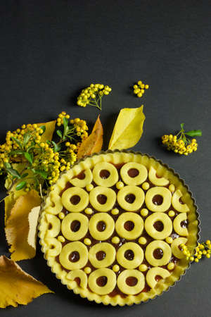 round pastry cake in baking pan ready for cooking, dry yellow leaves and berries on black background, copy space, verticalの写真素材