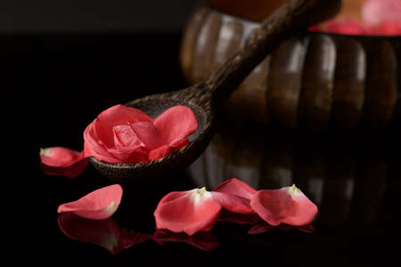 wooden ladle and bowl full of pink rose petals on reflected black background, concept of beautyの写真素材