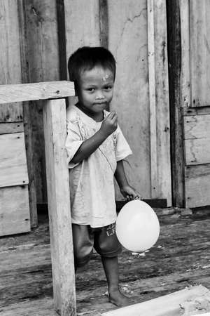 Togian islands, Indonesia - September 05, 2014: portrait of young boy of the village of sea gypsies with a balloon in his hand near stilt house, Sulawesi, black and whiteのeditorial素材