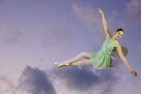 female ballet dancer sitting on cloud in dragonfly green costume, sky and clouds backgroundの写真素材