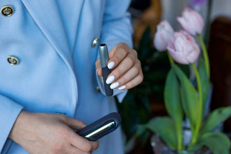 woman in blue jacket with electronic cigarette and charger in the handsの写真素材