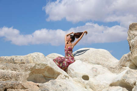 young woman in summer dress playing with her hair sitting on white rock in summer dayの写真素材