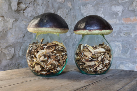 two glass jars filled with dried mushrooms on old wooden table, stone wall backgroundの写真素材