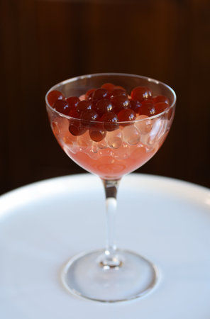 cocktail glass with strawberry bubble tea obtained with inverse spherification, brown backgroundの写真素材