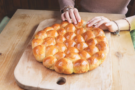 woman hands tearing off a piece of danube savory cake on wooden cutting board