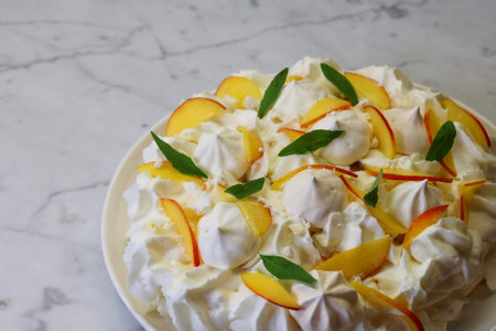 meringue dessert decorated with whipped cream and peach slices on narble tableの写真素材