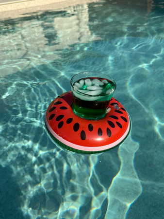 fresh drink floating in a funny inflatable in the shape of watermelon on a pool waterの写真素材