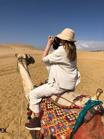 woman on camel photographing landscape of sahara desert, verticalの写真素材